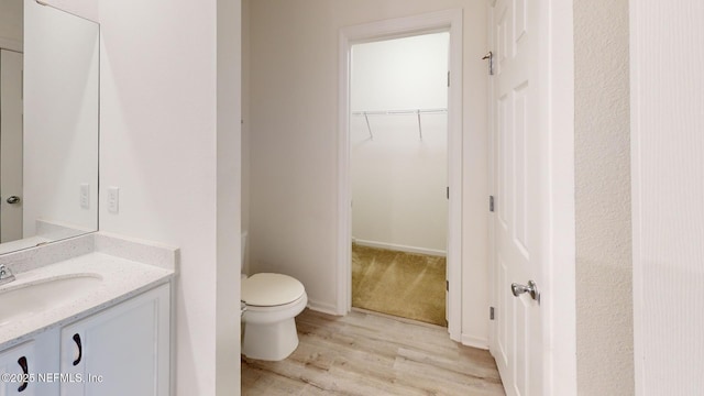 bathroom featuring toilet, a spacious closet, wood finished floors, and vanity