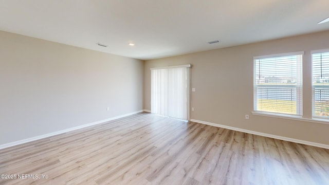 unfurnished room with light wood-type flooring, visible vents, and baseboards