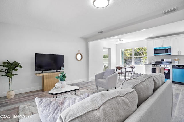 living room featuring baseboards, a textured ceiling, visible vents, and light wood-style floors