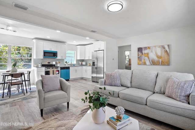 living room featuring light wood-style floors, recessed lighting, visible vents, and a textured ceiling