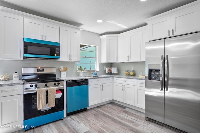 kitchen with tasteful backsplash, light wood-style flooring, appliances with stainless steel finishes, white cabinetry, and light stone countertops