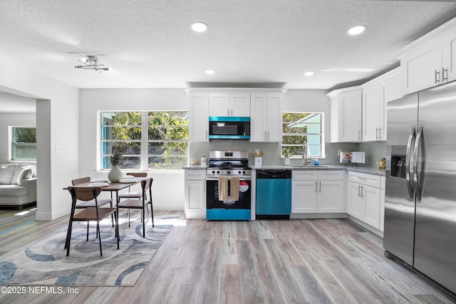 kitchen featuring light wood finished floors, tasteful backsplash, appliances with stainless steel finishes, white cabinets, and a sink