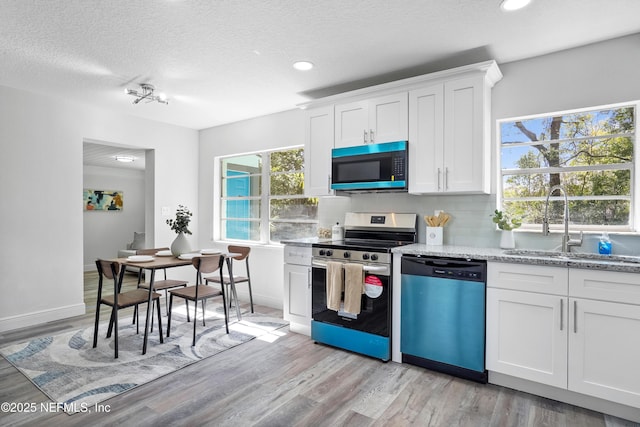 kitchen featuring dishwashing machine, light wood-style flooring, a sink, decorative backsplash, and stainless steel range with electric stovetop