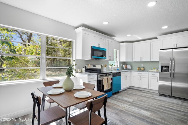 kitchen with a textured ceiling, white cabinetry, appliances with stainless steel finishes, light wood-type flooring, and tasteful backsplash