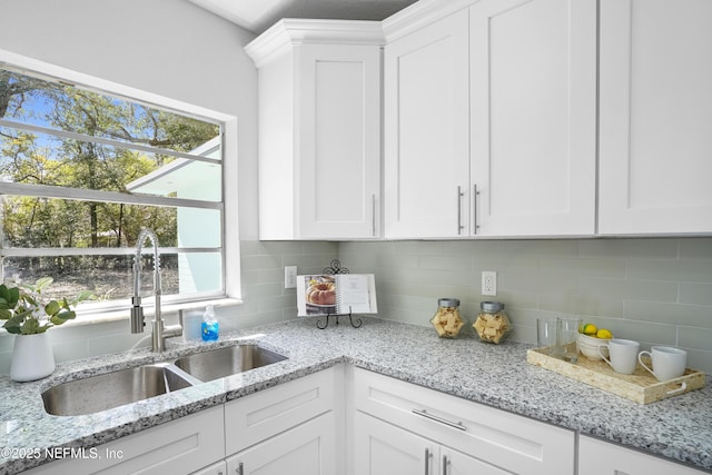 kitchen with light stone counters, white cabinetry, backsplash, and a sink