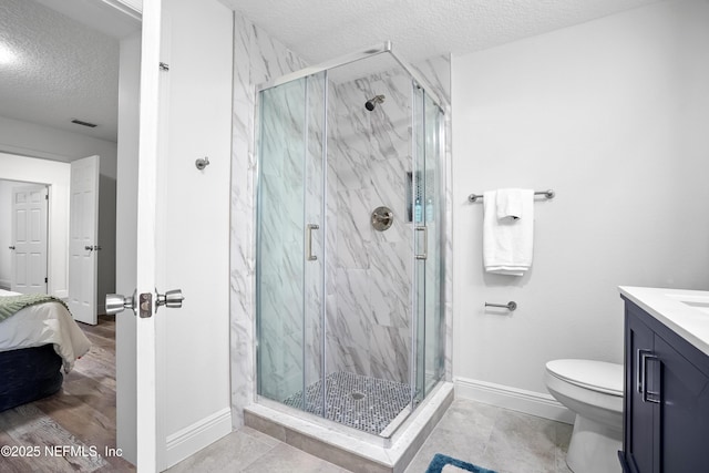 ensuite bathroom with a marble finish shower, baseboards, toilet, a textured ceiling, and vanity