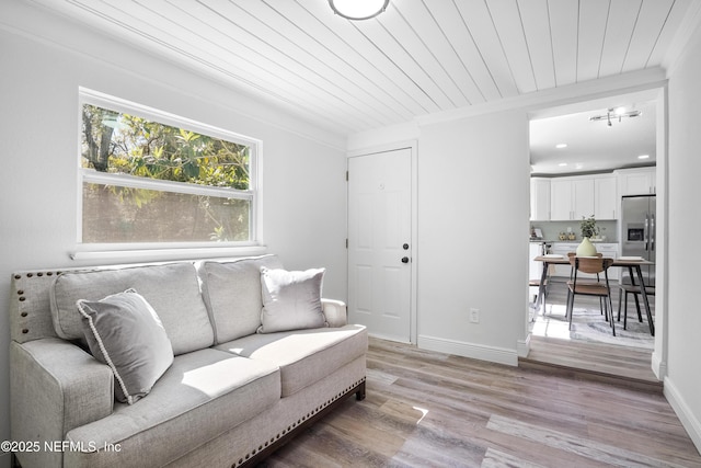 living area featuring baseboards, light wood-type flooring, wooden ceiling, and crown molding