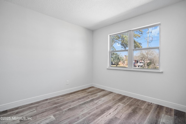 unfurnished room with a textured ceiling, wood finished floors, and baseboards