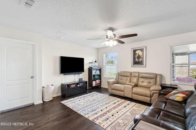 living area with a textured ceiling, dark wood finished floors, visible vents, and baseboards