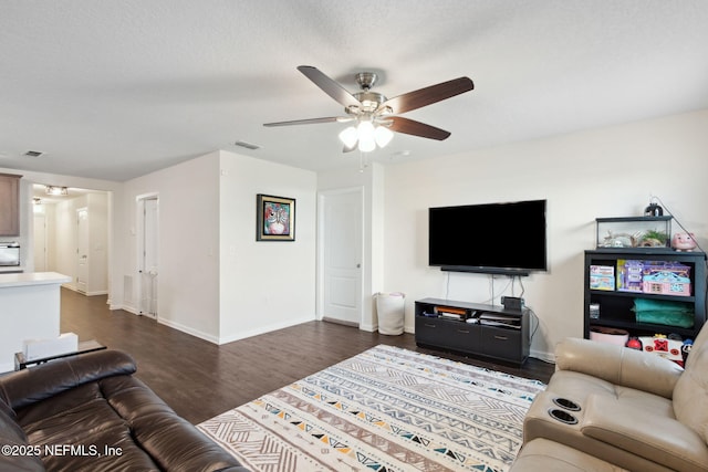 living room with dark wood-type flooring, visible vents, ceiling fan, and baseboards