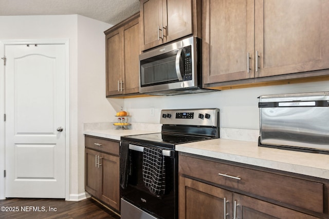 kitchen featuring a textured ceiling, light countertops, appliances with stainless steel finishes, and dark wood-style flooring