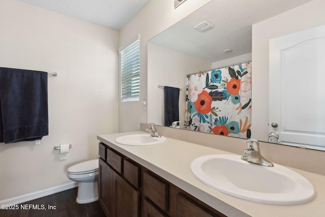 full bathroom with wood finished floors, a sink, toilet, and double vanity