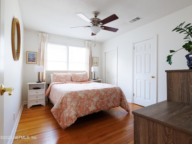 bedroom featuring a textured ceiling, hardwood / wood-style floors, visible vents, and baseboards