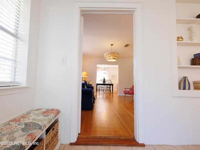 hall with light wood-type flooring, built in shelves, and visible vents