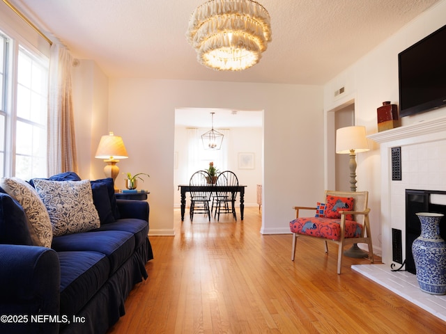 living area featuring light wood finished floors, visible vents, a tile fireplace, a textured ceiling, and a notable chandelier