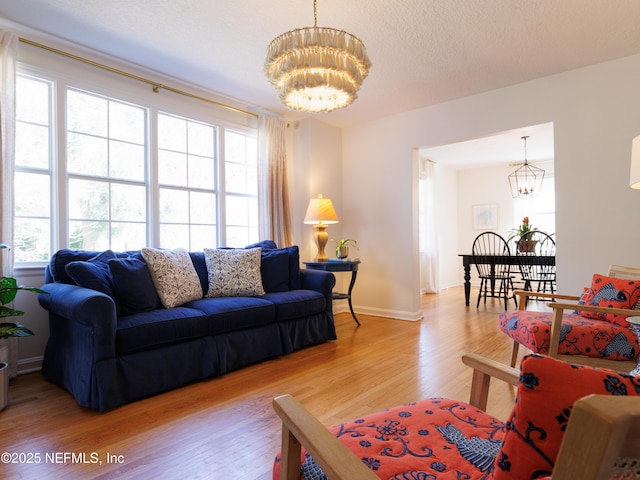 living room featuring baseboards, a textured ceiling, light wood-style flooring, and a notable chandelier