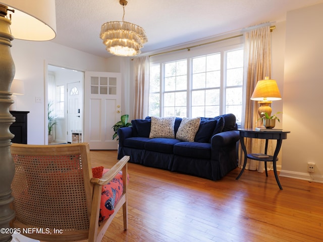 living room featuring a notable chandelier, a textured ceiling, baseboards, and wood finished floors