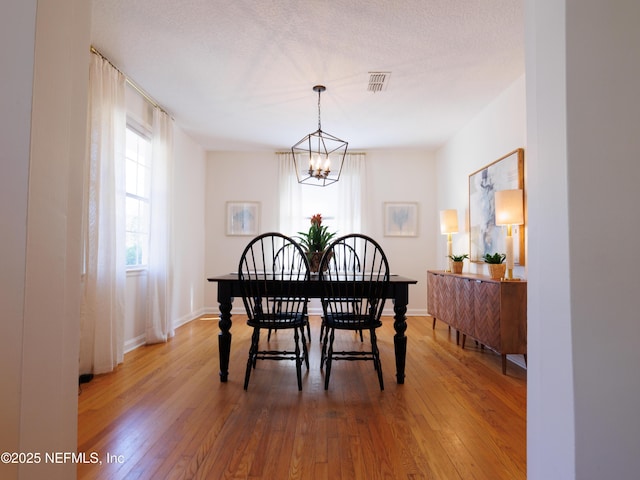 dining area featuring baseboards, visible vents, hardwood / wood-style flooring, an inviting chandelier, and a textured ceiling