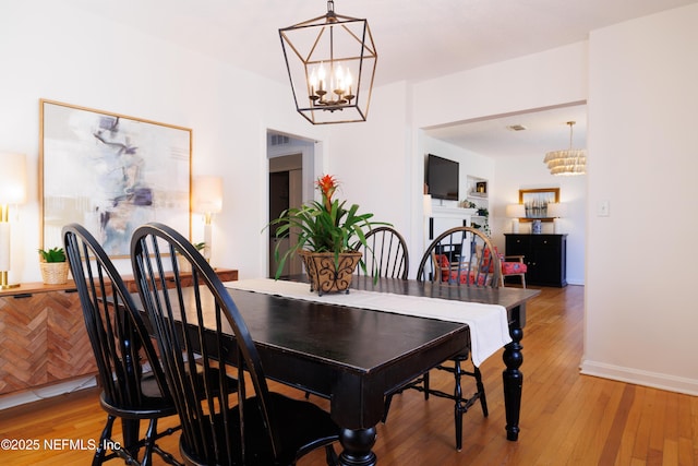 dining space with baseboards, light wood finished floors, and a notable chandelier