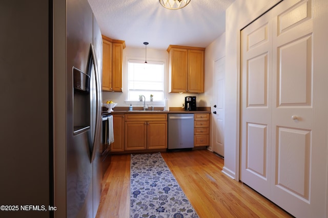 kitchen featuring decorative light fixtures, stainless steel appliances, dark countertops, light wood-style flooring, and a sink