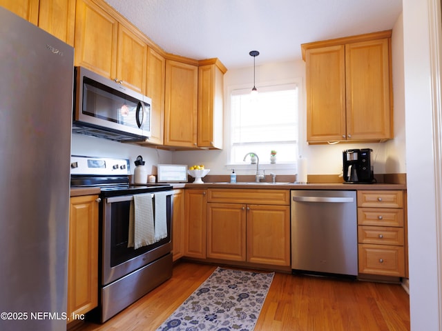 kitchen featuring dark countertops, wood finished floors, decorative light fixtures, stainless steel appliances, and a sink