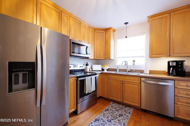 kitchen featuring light wood-style flooring, appliances with stainless steel finishes, a sink, and decorative light fixtures