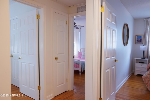 corridor with light wood-type flooring, baseboards, and visible vents