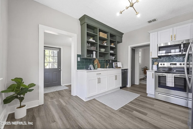 kitchen with wood finished floors, stainless steel appliances, light countertops, open shelves, and a sink