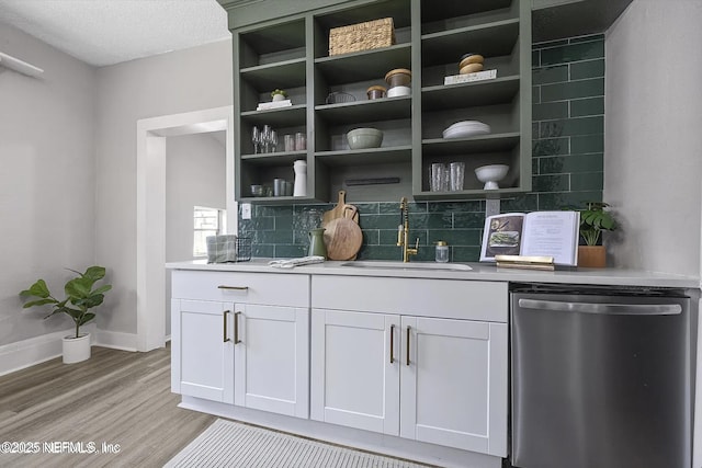 bar with tasteful backsplash, baseboards, light wood-style flooring, stainless steel dishwasher, and a sink