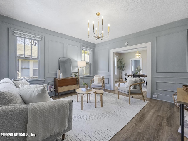 living area with a wealth of natural light, wood finished floors, a decorative wall, and an inviting chandelier