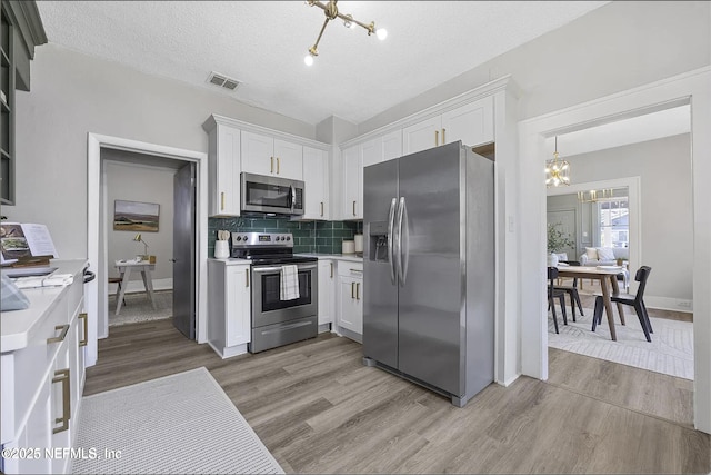 kitchen with light countertops, appliances with stainless steel finishes, white cabinetry, and a notable chandelier