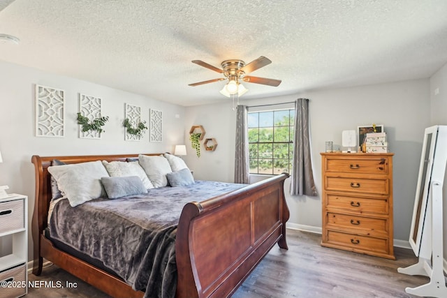 bedroom featuring ceiling fan, a textured ceiling, baseboards, and wood finished floors