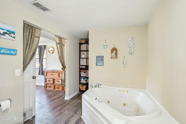 bathroom featuring a jetted tub, visible vents, a textured ceiling, and wood finished floors