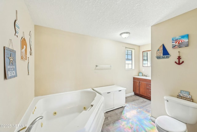 full bath with a textured ceiling, toilet, wood finished floors, vanity, and a jetted tub