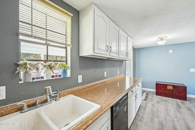 kitchen with a textured ceiling, a sink, white cabinetry, black dishwasher, and light wood finished floors