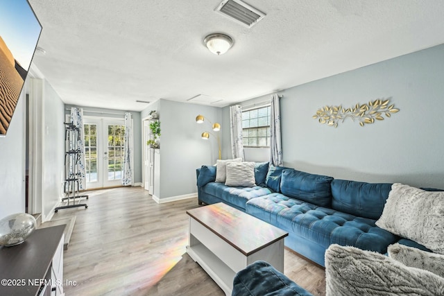 living area with french doors, visible vents, a textured ceiling, wood finished floors, and baseboards