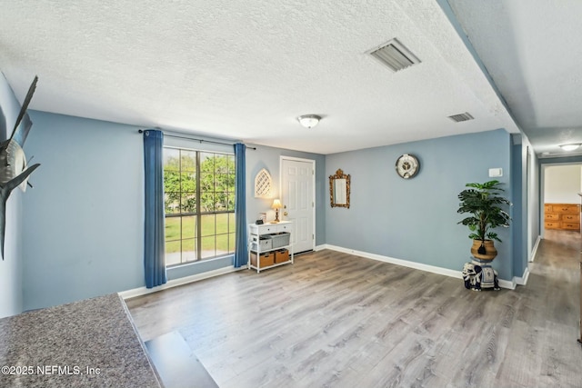 unfurnished room with a textured ceiling, wood finished floors, visible vents, and baseboards