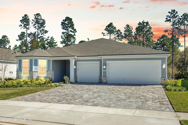 view of front facade with a garage, stone siding, a shingled roof, and decorative driveway