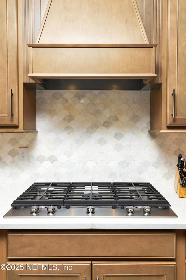 kitchen featuring tasteful backsplash, custom range hood, light countertops, and stainless steel gas stovetop