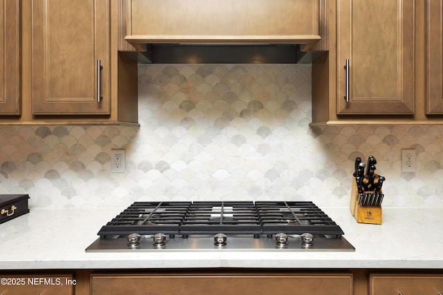 kitchen with light stone countertops, wall chimney range hood, tasteful backsplash, and stainless steel gas cooktop