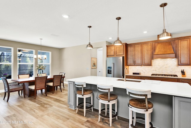 kitchen featuring tasteful backsplash, appliances with stainless steel finishes, custom exhaust hood, light countertops, and a sink