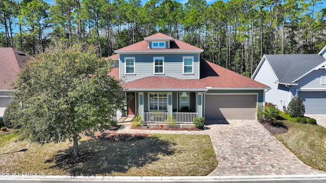 view of front of home featuring decorative driveway, a shingled roof, covered porch, a front yard, and an attached garage