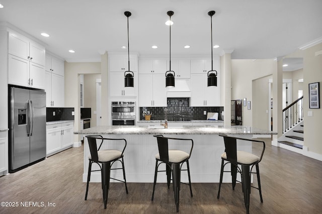 kitchen with ornamental molding, appliances with stainless steel finishes, wood finished floors, white cabinets, and a kitchen island with sink