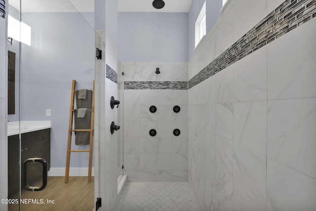 bathroom with baseboards, tiled shower, and wood finished floors
