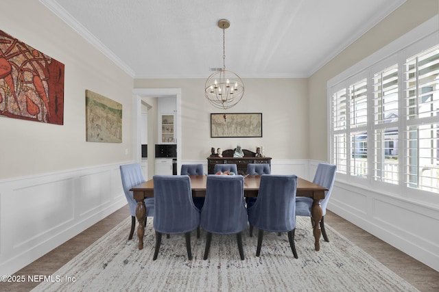 dining area with a notable chandelier, wood finished floors, wainscoting, and ornamental molding
