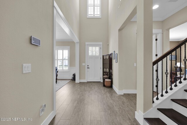 foyer entrance with wood finished floors, baseboards, stairs, a towering ceiling, and crown molding