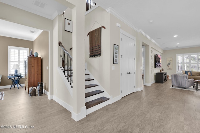 stairway with visible vents, plenty of natural light, wood finished floors, and ornamental molding