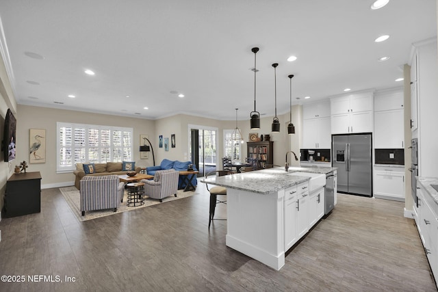 kitchen with a kitchen island with sink, ornamental molding, stainless steel appliances, light wood-style floors, and open floor plan
