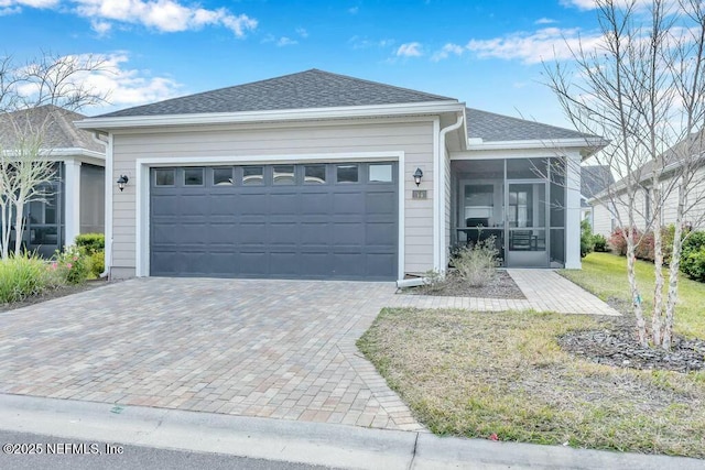 single story home featuring a garage, a sunroom, and roof with shingles