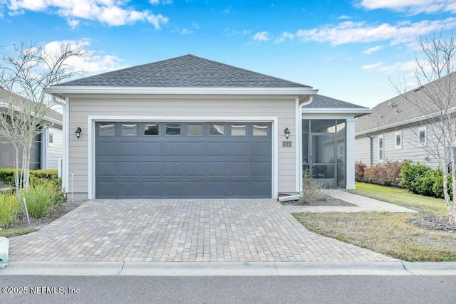 single story home with a garage, a shingled roof, decorative driveway, and a sunroom